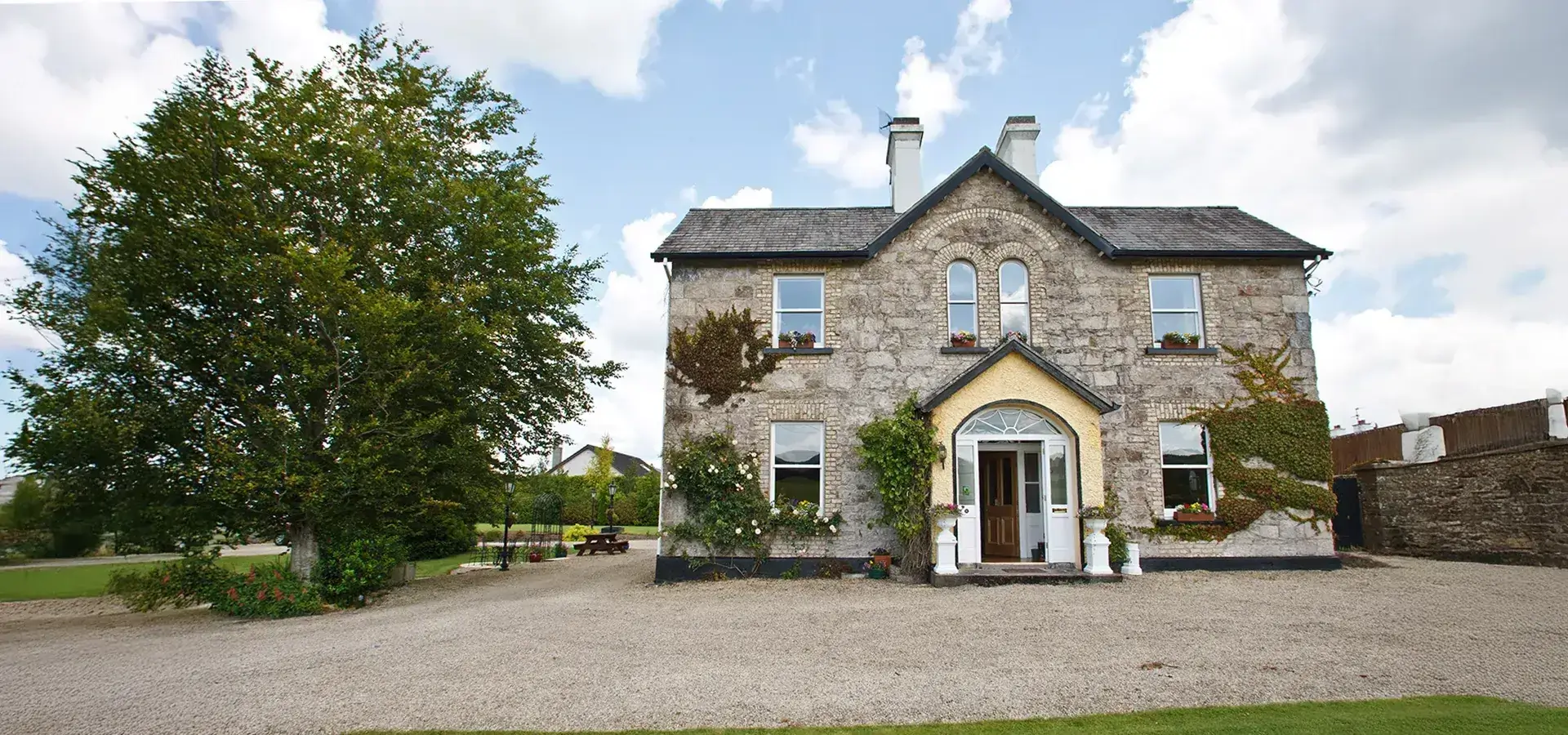A charming stone house with a yellow entrance, surrounded by greenery and flower pots. The History of Ardmore House Kinnitty Offaly