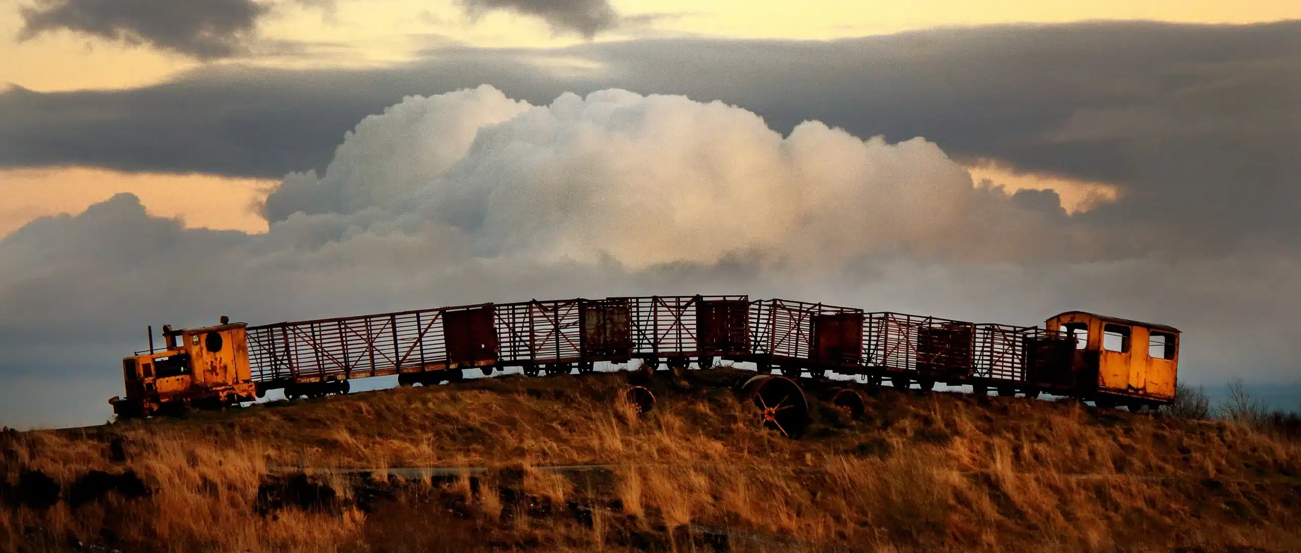 A classic vintage train with freight cars passing through a cloudy sunset sky