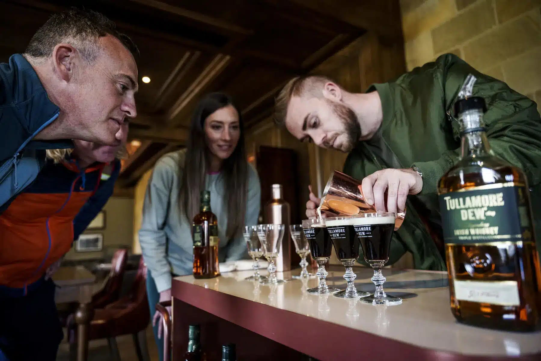 A group observes a bartender pouring drinks into glasses labeled Tullamore DEW